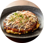 Okonomiyaki som er en japansk pandekage bestående af kål og æg krydret med barbeque-sovs pyntet med dressing og grøn topping